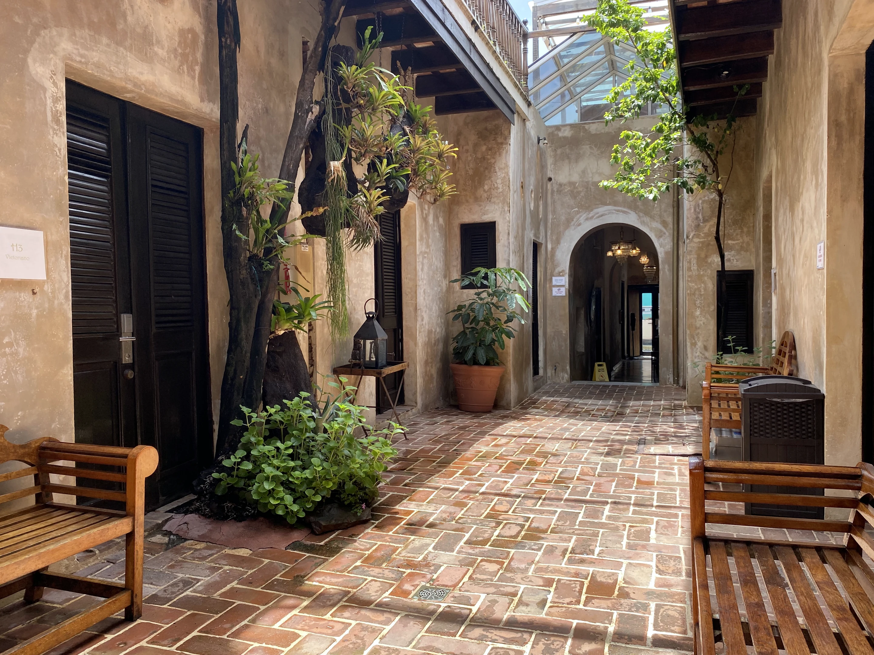 Sunlit Old San Juan courtyard with textured plaster, timber shutters, plants and brick paving